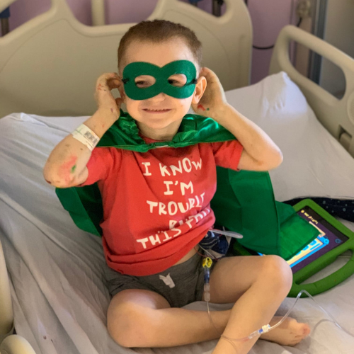 little boy in hospital bed with superhero cape and mask