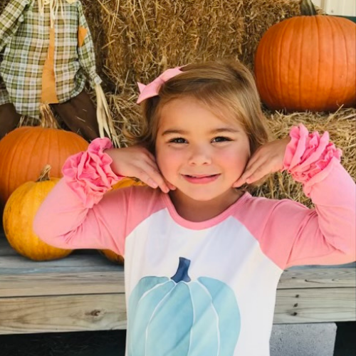 little girl smiling in front of pumpkins
